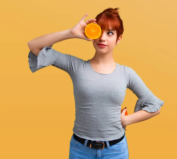 Turuncu zemin üzerine gözlük olarak portakal dilimleri giyen genç Kızıl saçlı kız