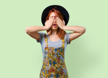 Gözleri eller tarafından kapsayan şapka ile serin Kızıl saçlı kız