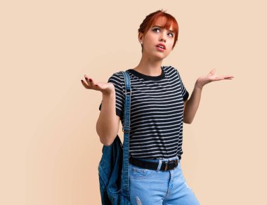 Genç öğrenci Kızıl saçlı kız şüpheleri ve koyu sarı arka plan üzerinde karıştırmayın yüz ifadesi ile