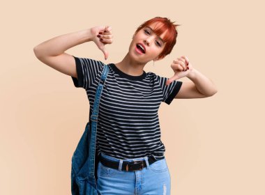 Başparmak aşağı işareti negatif ifade ile koyu sarı arka plan üzerinde gösterilen genç öğrenci Kızıl saçlı kız