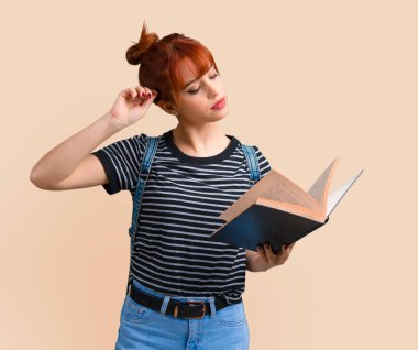 Bir kitap okuma ve koyu sarı arka plan üzerinde düşünme genç öğrenci Kızıl saçlı kız