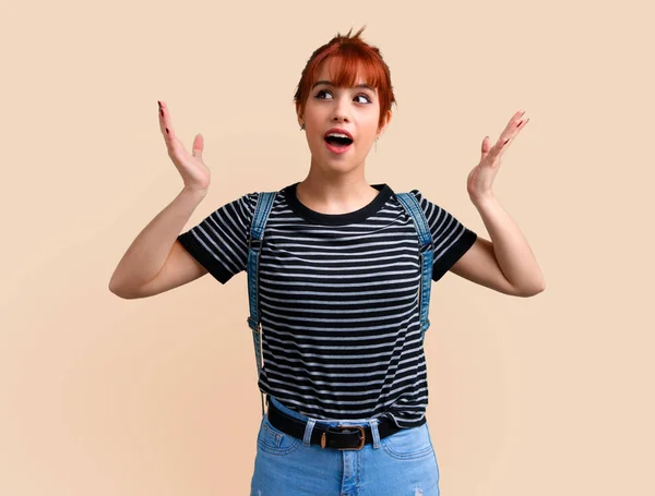 Young student redhead girl with surprise and shocked facial expression on ocher background