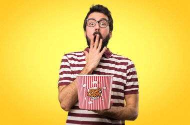 Şaşırmış adam gözlüklü popcorns renkli arka plan üzerinde yemek
