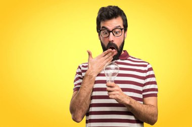 Gözlüklü bir ampul renkli arka plan üzerinde tutarak şaşırmış adam