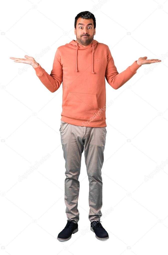 Full body of Man in a pink sweatshirt having doubts and with confuse face expression while raising hands and shoulders on isolated white background