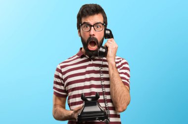 Renkli arka plan üzerinde konuşmak için vintage telefon gözlüklü şaşırmış adam