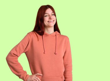 Silah, kalça ile poz ve yeşil arka plan üzerinde gülümseyen pembe kazak ile genç Kızıl saçlı kız