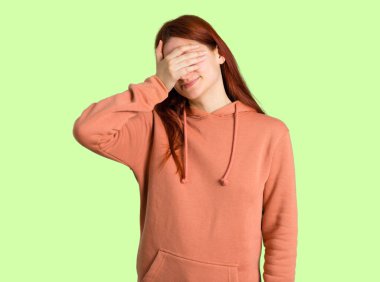 Pembe kazak gözleri eller tarafından kapsayan genç Kızıl saçlı kız. Bir şey yeşil arka plan üzerinde görmek istiyor musunuz