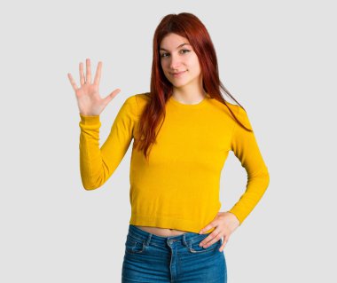 Genç Kızıl saçlı kız sarı kazaklı beş ile gri arka plan üzerinde parmak sayma