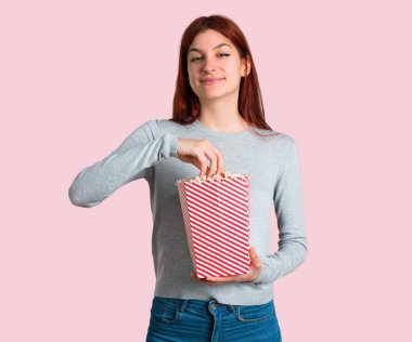 Popcorns izole pembe bir arka plan üzerinde büyük bir kase içinde yeme genç Kızıl saçlı kız