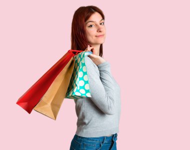 Bir sürü alışveriş torbaları izole pembe arka plan üzerinde tutan genç Kızıl saçlı kız