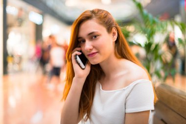 Cep telefonu ile bir görüşme biriyle tutmak bir alışveriş merkezinde genç Kızıl saçlı güzel kız