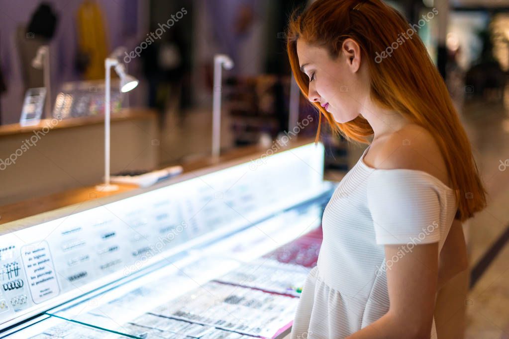 Young redhead pretty girl in a shopping center looking at jewelry
