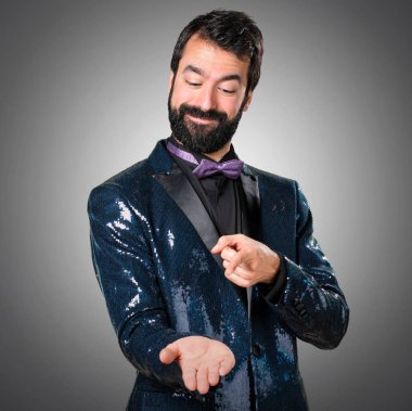 Bir şey gri arka plan üzerinde tutan payet ceket ile yakışıklı adam
