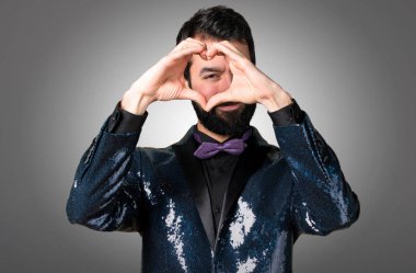 Yakışıklı adamla payet ceket gri arka plan üzerinde elleriyle bir kalp yapma