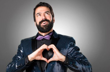 Yakışıklı adamla payet ceket gri arka plan üzerinde elleriyle bir kalp yapma