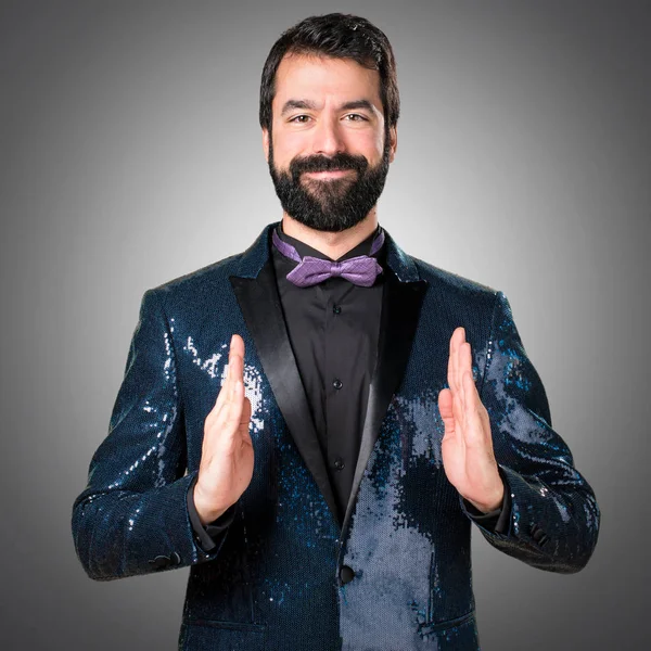 Bir şey gri arka plan üzerinde tutan payet ceket ile yakışıklı adam