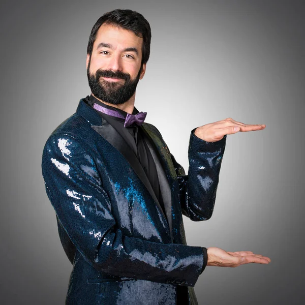 Bir şey gri arka plan üzerinde tutan payet ceket ile yakışıklı adam