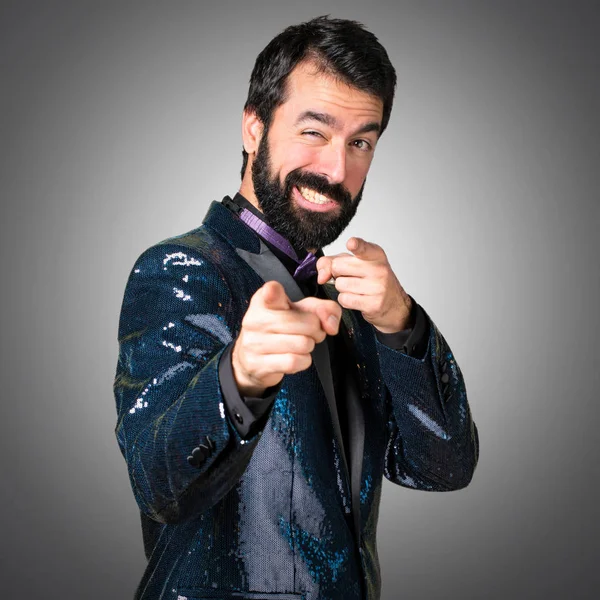 Handsome man with sequin jacket pointing to the front on grey background