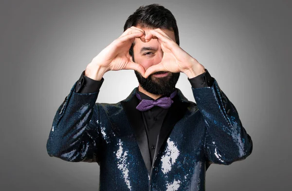 Yakışıklı adamla payet ceket gri arka plan üzerinde elleriyle bir kalp yapma