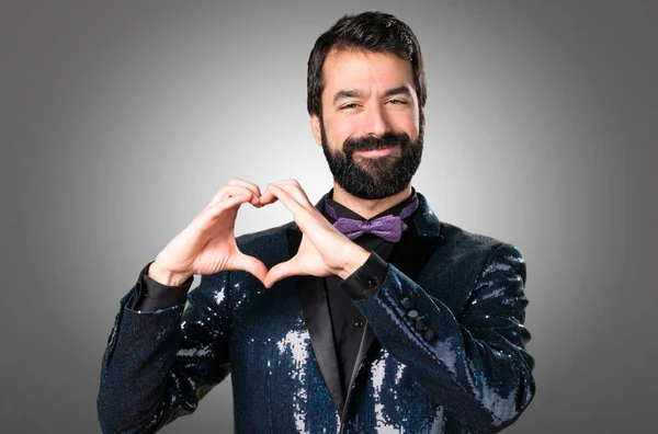 Yakışıklı adamla payet ceket gri arka plan üzerinde elleriyle bir kalp yapma