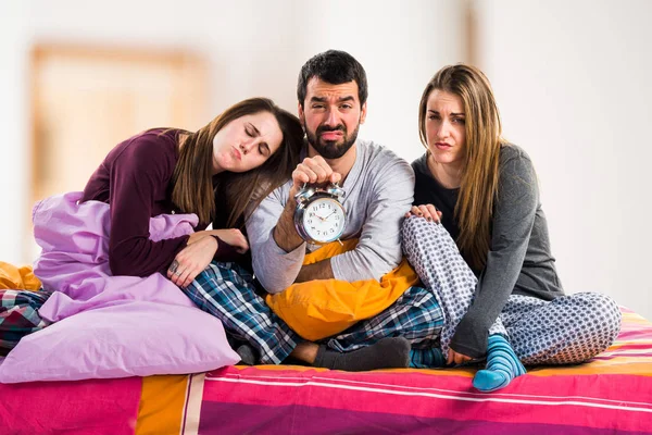 Three friends on a bed holding vintage clock