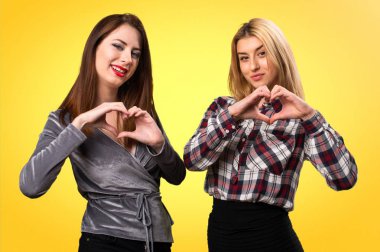 İki arkadaş renkli arka plan üzerinde kendi elleriyle bir kalp yapma