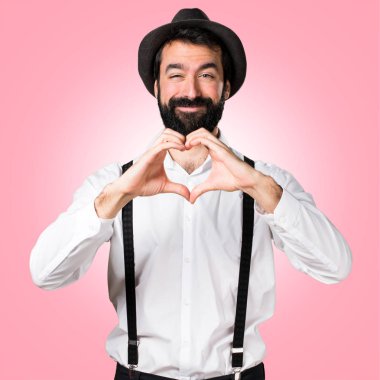 Renkli arka plan üzerinde bir kalp elleriyle yapma sakallı hippi adam