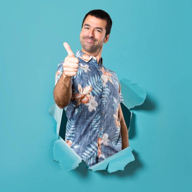 Çiçek gömlek ile bir mavi kağıt delikten başparmak ile yakışıklı adam