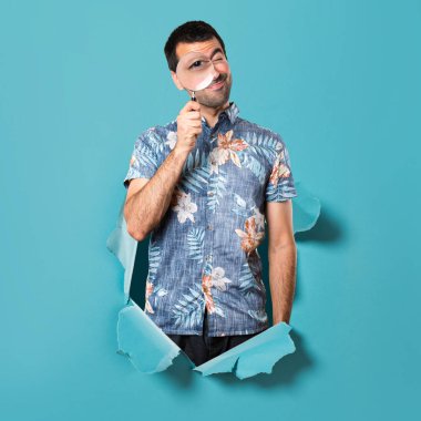 Büyüteç bir mavi kağıt delikten ile çiçek forması ile yakışıklı adam