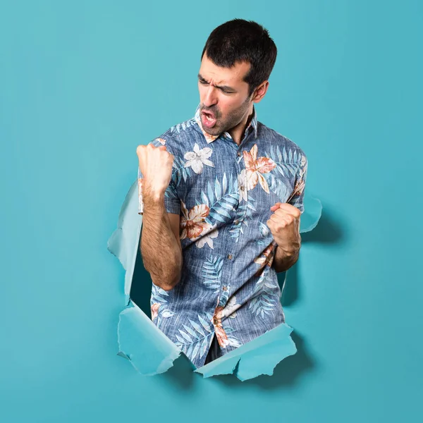 Lucky handsome man with flower shirt through a blue paper hole