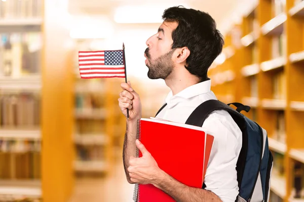 Student man holding an american flag on defocused library