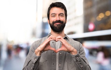 Elleri ile bir kalp, açık hale sakallı yakışıklı adam