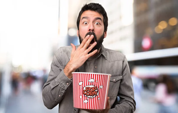 Surprised Handsome man with beard eating popcorns at outdoor