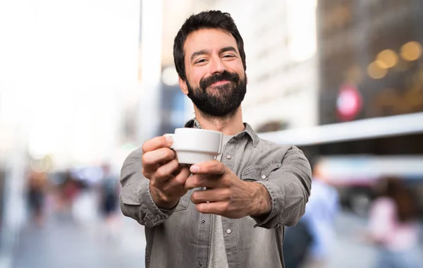 Handsome man with beard holding a cup of coffee at outdoor