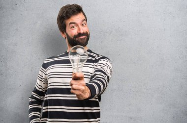 Sakallı bir ampul dokulu arka plan üzerinde tutan mutlu adam