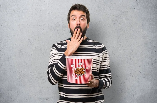 Surprised Man with beard eating popcorns on textured background