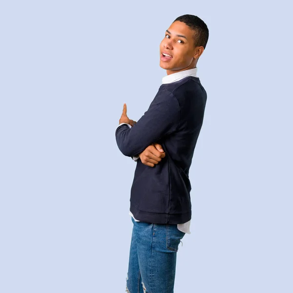 Young african american man pointing back with the index finger on isolated blue background