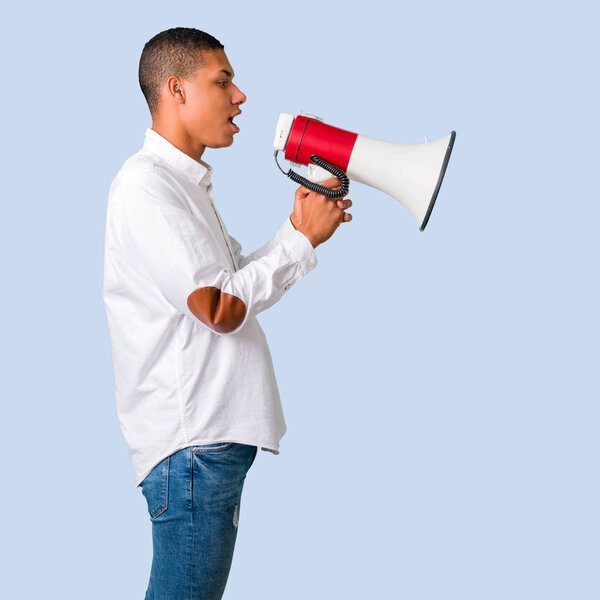 Молодой африканский американец в белой рубашке кричит через мегафон, чтобы объявить что-то в боковом положении на изолированном синем фоне
