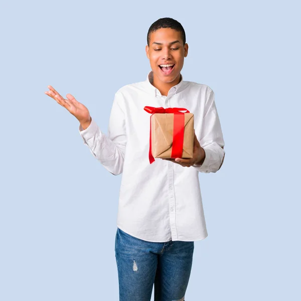 年轻的非洲裔美国男子与白色衬衫惊讶 因为已经得到了一个独立的蓝色背景礼物 — 图库照片