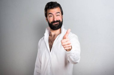Gri arka plan üzerinde başparmak ile sakallı yakışıklı adam