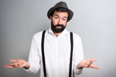 Gri arka plan üzerinde önemsiz jest yapma sakallı hippi adam