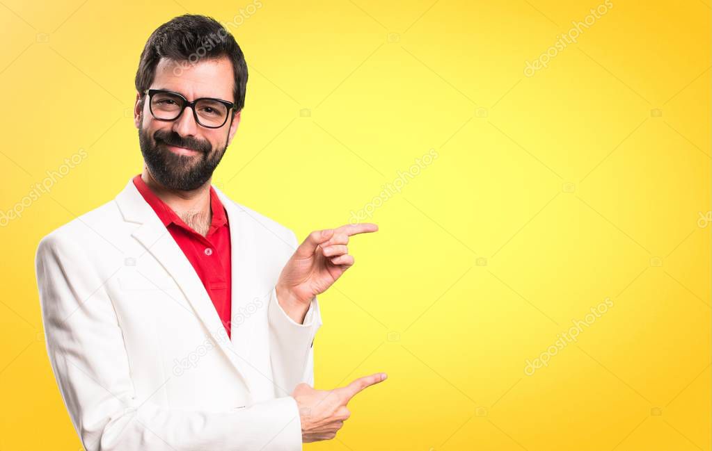 Brunette man with glasses pointing to the lateral on colorful background