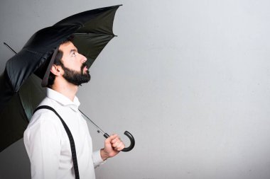 Gri arka plan üzerinde bir şemsiye tutan sakallı hippi adam