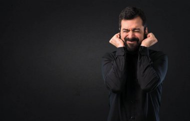 Kulakları siyah arka plan üzerine kapsayan sakallı yakışıklı adam