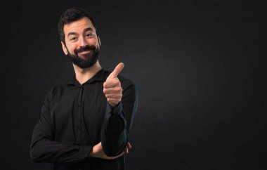 Siyah arka plan üzerine başparmak ile sakallı yakışıklı adam