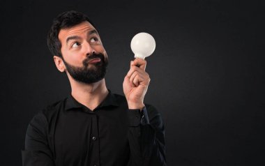 Bir ampul siyah arka plan üzerine tutarak sakallı yakışıklı adam