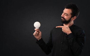 Bir ampul siyah arka plan üzerine tutarak sakallı yakışıklı adam