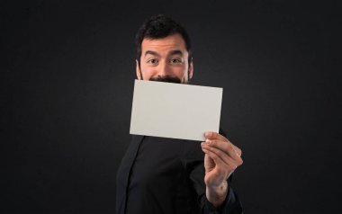 Boş bir afişini siyah arka plan üzerine tutarak sakallı yakışıklı adam