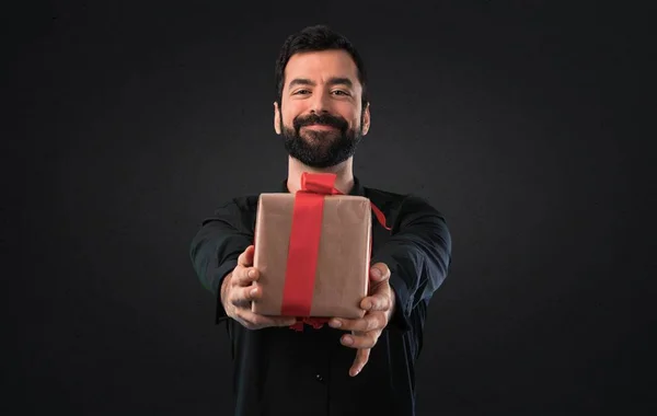 Handsome man with beard holding a gift on black background